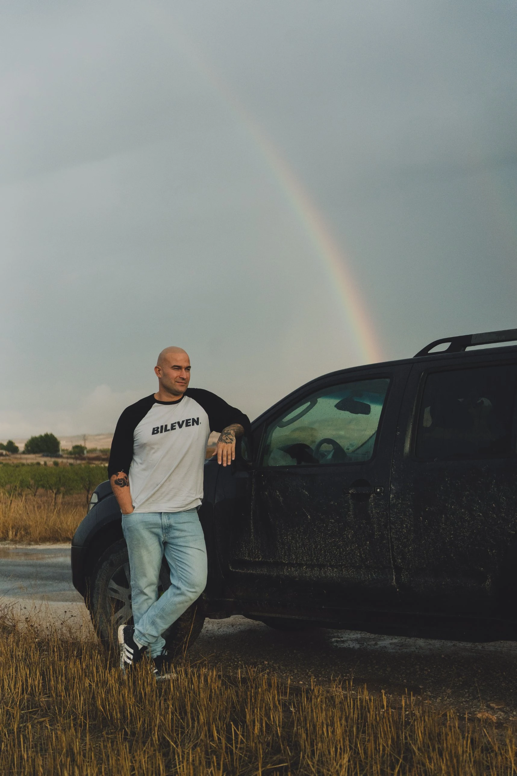 Él apoyado en la pick-up con el arcoíris al fondo