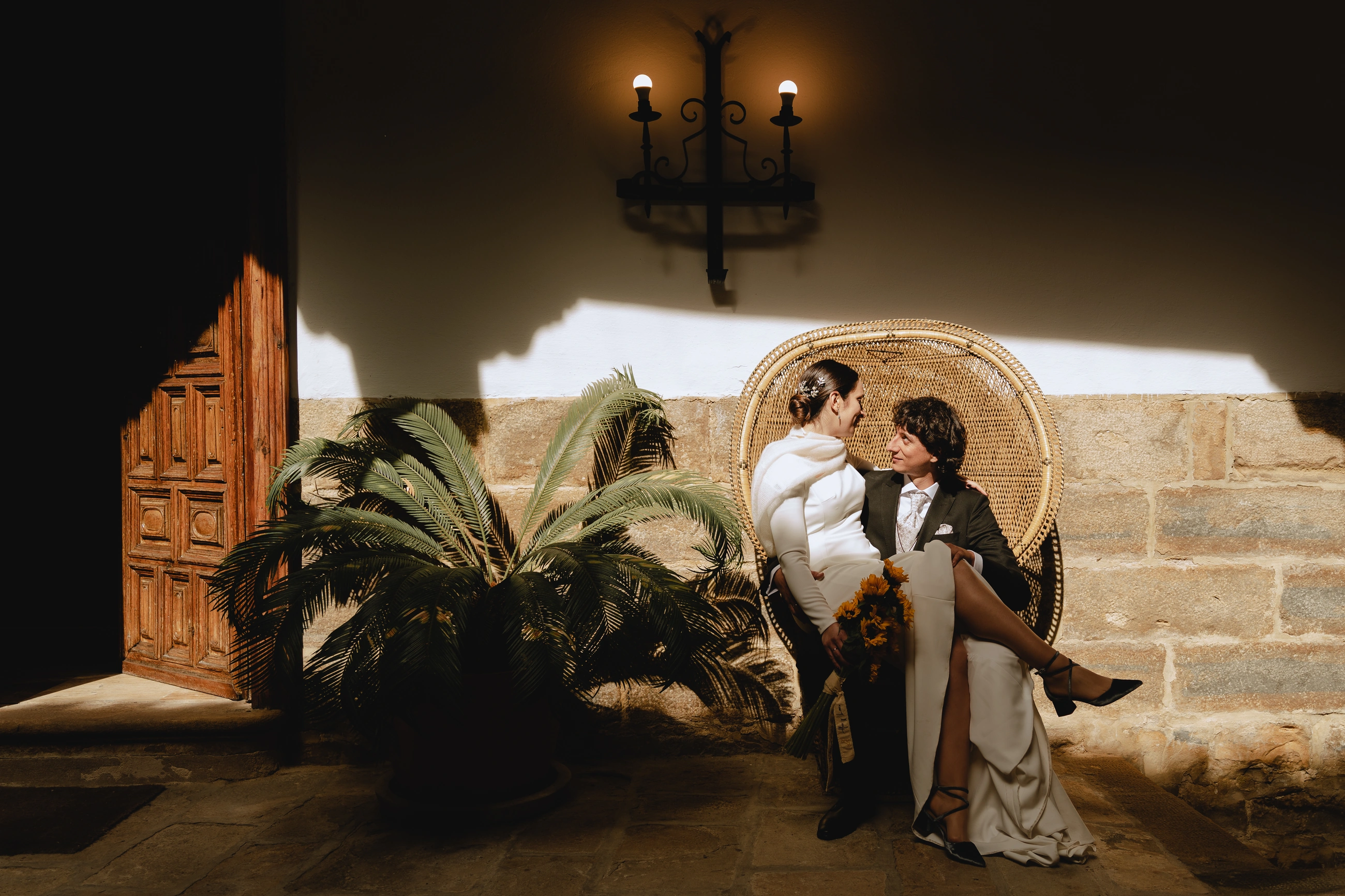 Los novios sentados en el sillón de mimbre, contra el muro de piedra